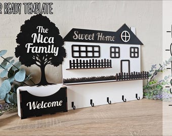 May include: A laser cut wooden key holder with a house design and the text "Sweet Home". The house has a black fence and a black tree with the text "The Nica Family". The key holder has a black welcome sign and five hooks.