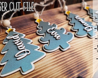 May include: Laser cut file for Christmas tree ornaments with the text LASER CUT FILE, DXF, CDR, PDF, SVG, AI. The ornaments are teal, layered wood shapes with white script names like David and Eva, topped with a small yellow star and wooden bead.