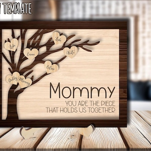 Könnte beinhalten: Ein lasergeschnittenes Holzschild mit einem Baumdesign und Herzen. Die Herzen haben Namen darauf geschrieben, darunter "Mommy", "Daddy", "Emma", "Celine", "Luke" und "Kat". Das Schild lautet "Mommy, you are the piece that holds us together".