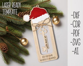 May include: A wooden Christmas ornament with a Santa hat design. The ornament features a key labeled "Santa's Magic Key" and the text "For our home without a chimney." The ornament is surrounded by pine branches, gold ornaments, and a pine cone.