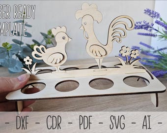 May include: Laser cut wooden egg holder with a rooster and hen design. The holder has six slots for eggs and a base with two legs. The text "LASER READY TEMPLATE" is at the top of the image.