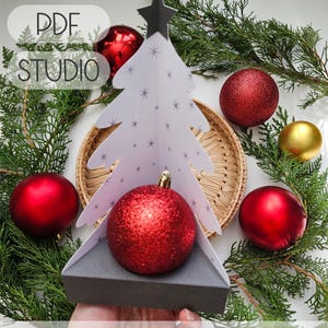 May include: A white paper Christmas tree with star accents and a black star topper, holding a red glitter ornament. The image includes red and gold ornaments, greenery, and the text "SVG PDF STUDIO". Compatible ornament size: 2.55 to 2.75 inches in diameter.
