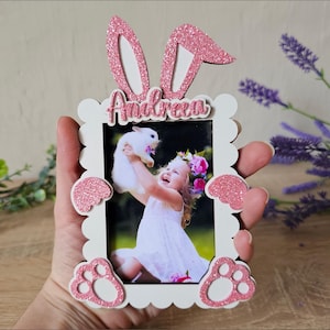 Könnte beinhalten: Ein weißer Fotorahmen mit rosa Glitzer-Hasenohren, Pfoten und Akzenten, der ein Foto eines Kindes mit einem Hasen enthält. Der Name "Andreea" befindet sich über dem Foto. Der Rahmen ist eine lasertaugliche Vorlage.
