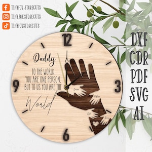 May include: A wooden clock with a brown handprint design and the text "Daddy to the world you are one person, but to us you are the world". The clock face has black numbers and hands.