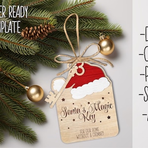 Könnte beinhalten: Ein hölzerner Weihnachtsanhänger in Form eines Schlüssels mit einer Weihnachtsmannmütze oben drauf. Der Anhänger ist mit Sternen und dem Text "Santa's Magic Key" und "For our home without a chimney" verziert.