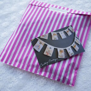 May include: A pink and white striped paper bag with a card inside. The card features a hand-stitched bunting with numbers 15 through 18 and the text "Crafty Boutique".