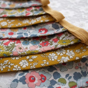 May include: A bunting banner with alternating yellow and floral fabric panels. The floral fabric features a white background with a variety of colorful flowers and leaves.