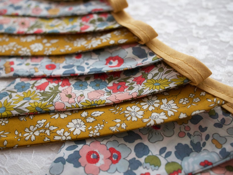 May include: A bunting banner with alternating yellow and floral fabric panels. The floral fabric features a white background with a variety of colorful flowers and leaves.