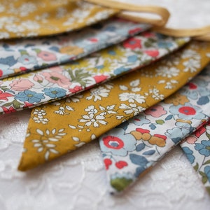 May include: A bunting banner with a yellow background and a floral pattern in shades of blue, pink, and red. The bunting is made of fabric and has a string for hanging.