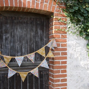 May include: A rustic wooden door with a brick archway and a floral patterned bunting hanging above it. The bunting is made of fabric triangles with a yellow trim. The door is weathered and has a dark brown finish.