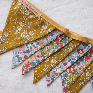 May include: A bunting banner with a yellow background and a floral pattern. The banner is made of fabric and has a white trim. The banner says " Bunting Boutique" on one of the flags.