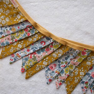 May include: A yellow and blue floral fabric bunting with a yellow trim. The bunting is made of triangular flags with a floral pattern.