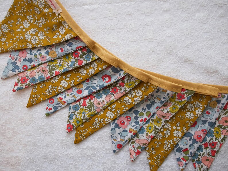 May include: A yellow and blue floral fabric bunting with a yellow trim. The bunting is made of triangular flags with a floral pattern.