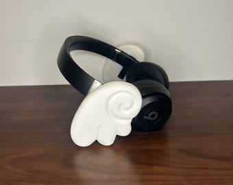 May include: Black over-ear headphones with a white wing-shaped accessory attached to the side.