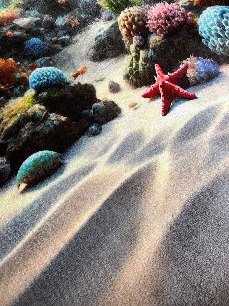May include: A fabric print featuring an underwater scene with a bright red starfish resting on light-colored sandy ocean floor. The composition includes dark rocks, vibrant blue and pink coral formations, and light patterns cast by water.