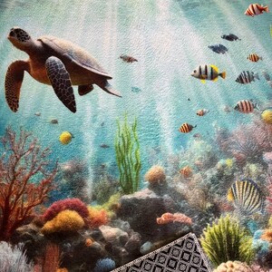 May include: A rectangular mat featuring an underwater scene with a sea turtle swimming among colorful coral reefs, green seaweed, and various small fish. The surface has a textured finish, and the underside shows a black and white geometric pattern.
