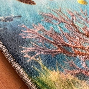 May include: A soft, plush area rug featuring a vibrant underwater scene with a brown sea turtle swimming above a detailed coral reef. The rug has a textured, fuzzy surface with a light blue, green, and brown color palette and a finished edge.