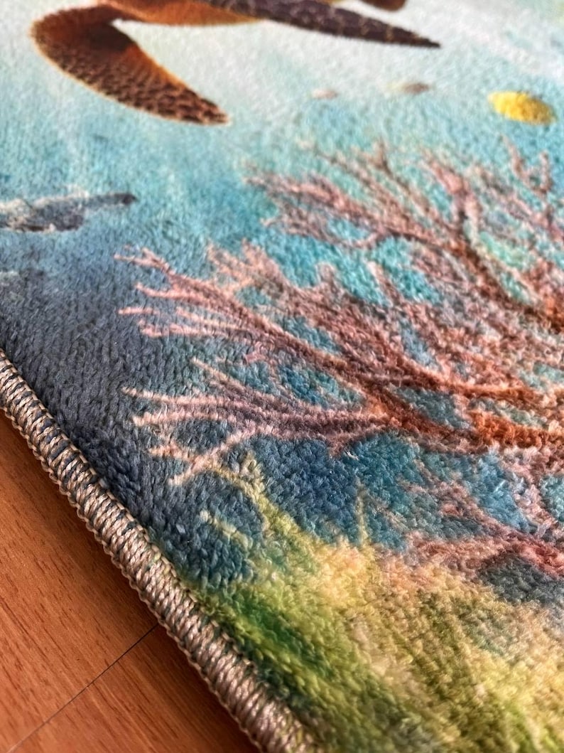 May include: A soft, plush area rug featuring a vibrant underwater scene with a brown sea turtle swimming above a detailed coral reef. The rug has a textured, fuzzy surface with a light blue, green, and brown color palette and a finished edge.