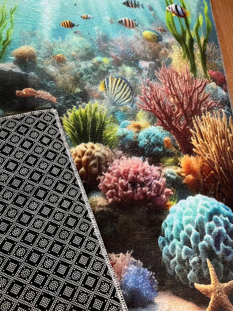 May include: A rectangular area rug featuring a vibrant underwater coral reef scene with colorful fish, various coral formations, and a starfish. The underside of the rug is black with a white geometric non-slip pattern and a stitched white border.