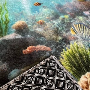 May include: A rectangular floor mat featuring a vibrant underwater coral reef scene with various colorful tropical fish, green seaweed, and textured rocks. The underside of the mat is black with a white geometric grid pattern and stitched edges.