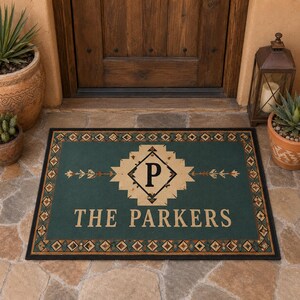 May include: A rectangular doormat with a dark teal background and a black border featuring a geometric pattern. The center displays a beige diamond shape with the letter P, flanked by arrows, and the text THE PARKERS in beige capital letters.