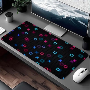 May include: Black rectangular gaming mouse mat featuring a pattern of colourful game controller symbols. The symbols include blue, pink, and purple circles, squares, and crosses. A white mouse is on the right.