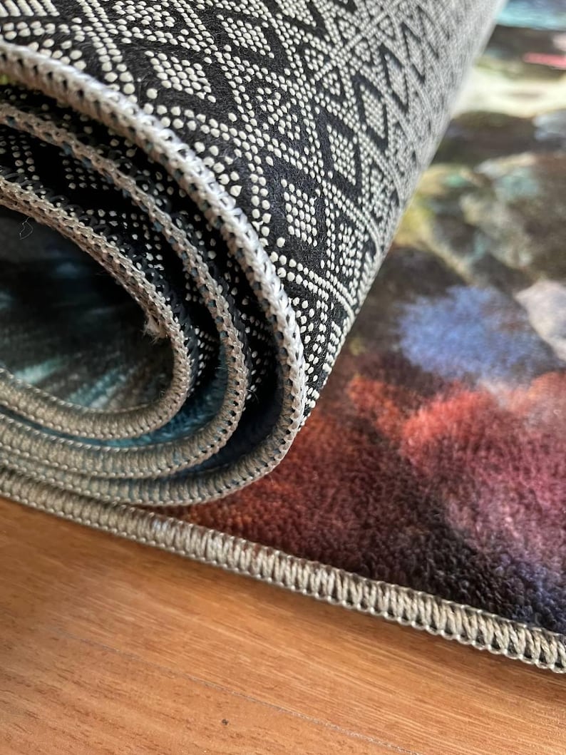 May include: A rolled area rug featuring a black underside with a white geometric diamond pattern and non-slip rubberized dots. The top surface displays a blurred, multi-colored abstract design in shades of deep red, blue, and dark tones.
