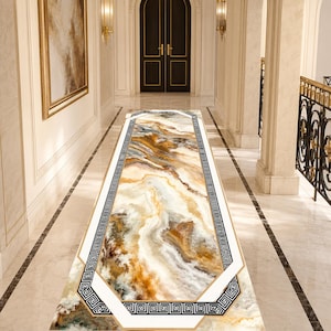 May include: A long rectangular runner rug featuring a marbled pattern in shades of cream, white, brown, and gold. The rug is bordered by a white frame and a black and white geometric Greek key pattern, creating a distinct visual contrast.