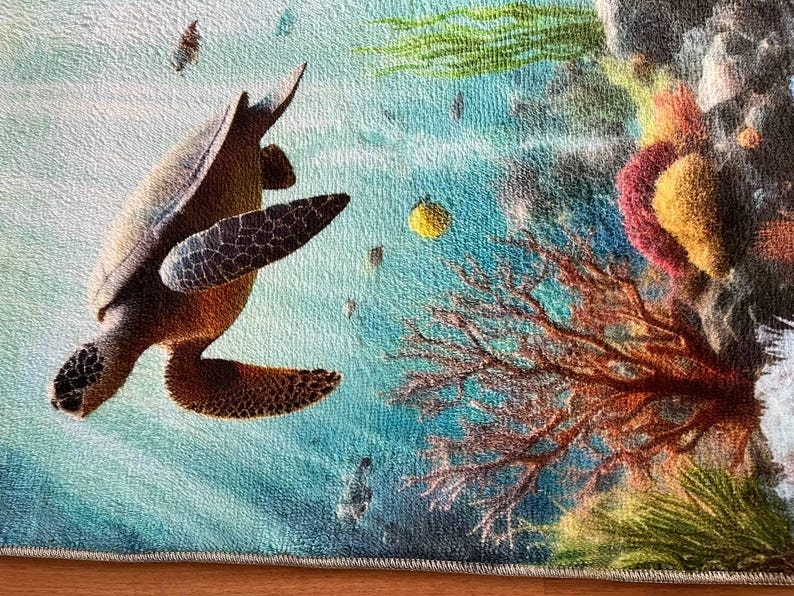 May include: A rectangular rug featuring a detailed underwater scene with a brown sea turtle swimming toward a vibrant coral reef. The reef displays shades of red, yellow, and green, set against a textured blue ocean background with small fish.