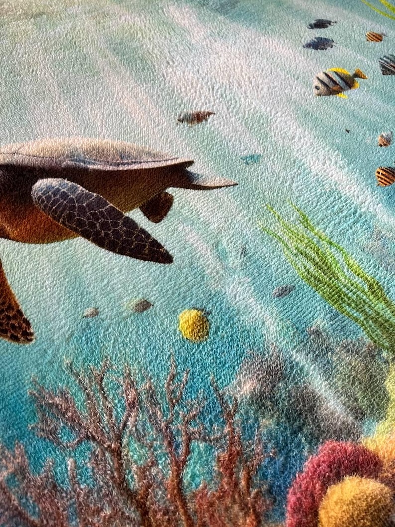 May include: A textured fabric print featuring an underwater scene with a brown sea turtle swimming through light blue water. The scene includes small colorful tropical fish, green seaweed, and brown coral formations at the bottom of the frame.