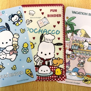 Puede incluir: Tres coloridas carpetas Fun con temática de Pochacco. La carpeta azul presenta a Pochacco con un cono de helado. La carpeta central tiene un Pochacco chef. La carpeta derecha es una carpeta de vacaciones con una escena de playa. Cada carpeta tiene el texto "Fun Binder" o "Vacation Binder".