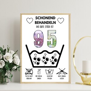Könnte beinhalten: Ein gerahmter Druck mit deutschem Text und Wäschezeichen. Der Text lautet "SCHONEND BEHANDELN" und "DAS GUTE STÜCK IST 95". Die Zahl 95 besteht aus Euro-Banknoten. Zu den Wäschezeichen gehören "Nicht bügeln", "Frischepflege", "Schonende Pflege" und "Nicht aufhängen".