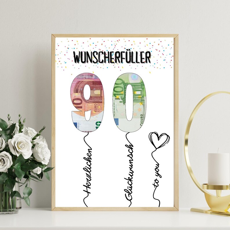 May include: A framed print with the number 90 formed from Euro banknotes. The text "Wunscherf&uuml;ller" is at the top, with "Herzlichen" and "Gl&uuml;ckwunsch to you" below. A heart is drawn on the right side.