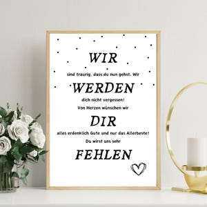 May include: A framed print with a light wood frame. The text in the print reads "WIR WERDEN DIR FEHLEN" in a black, bold font. A small heart is at the bottom right. The background is white with small black dots.