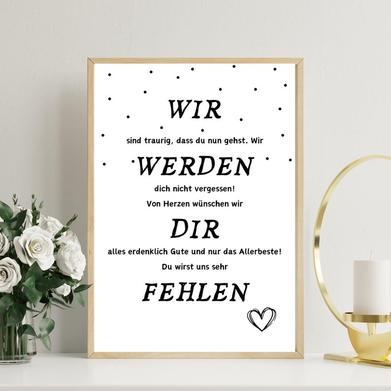 May include: A framed print with a light wood frame. The text in the print reads "WIR WERDEN DIR FEHLEN" in a black, bold font. A small heart is at the bottom right. The background is white with small black dots.