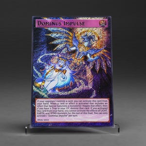 Könnte beinhalten: Eine holografische Sammelkarte mit dem Titel "Dominus Impulse" mit einem lebendigen Design, das eine geflügelte Figur in Blau und Gold zeigt. Die Karte enthält Text, der ihre Effekte beschreibt, und wird auf einem transparenten Ständer präsentiert.