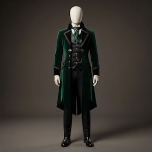 May include: A dark green velvet tailcoat featuring black lapel trim and gold buttons, worn over a black vest with a gold pocket watch chain, a green cravat with a central brooch, and black trousers on a faceless mannequin display.