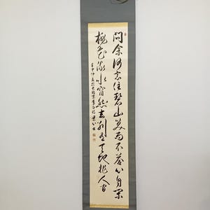 Peut inclure: Une calligraphie japonaise traditionnelle en noir sur fond crème. Le rouleau est monté sur un fond en tissu gris et possède un enrouleur en bois en haut et en bas. Le texte sur le rouleau est le suivant : "同余り忘住君山笑而不着いり京 極ひふ小宿無玄幻空了欠兆人す 在中中表款长国京李白漂いま"