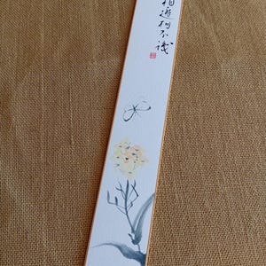 Puede incluir: Marcapáginas rectangular con fondo blanco y borde naranja fino. El marcapáginas presenta una mariposa y un diseño floral en acuarela. Caligrafía china escrita en la parte superior.