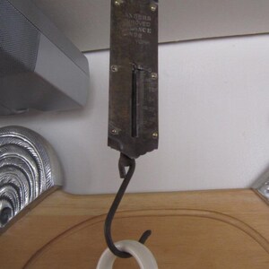 May include: A vintage metal hanging scale with a black hook and a white dial that reads "Sanders Improved Balance No. 1092".