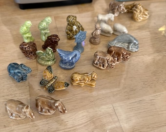 May include: A collection of small, ceramic animal figurines in various colors, including green, brown, blue, and tan. The figurines depict animals such as elephants, bears, and a butterfly. The figurines are arranged on a light-colored wooden surface.