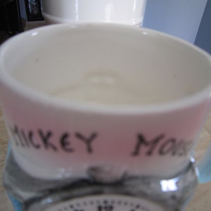 Puede incluir: Una taza de cer&aacute;mica rosa y azul con una imagen en blanco y negro de Mickey Mouse y el texto "Mickey Mouse" en el lateral.