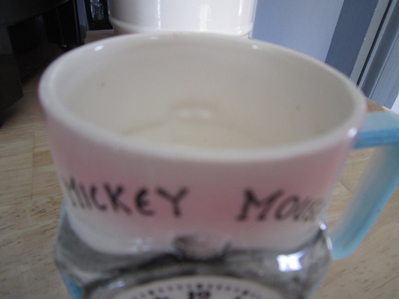 Puede incluir: Una taza de cer&aacute;mica rosa y azul con una imagen en blanco y negro de Mickey Mouse y el texto "Mickey Mouse" en el lateral.