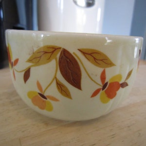 May include: A white ceramic bowl with a fall leaf pattern in shades of brown, orange, and yellow. The bowl has a scalloped rim and is perfect for serving snacks or desserts.