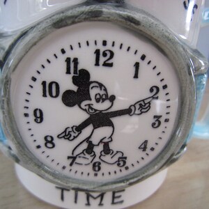 Puede incluir: Taza de cer&aacute;mica blanca con asa azul. La taza presenta una esfera de reloj de Mickey Mouse con las palabras "TIME" impresas debajo.