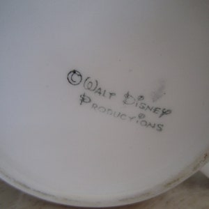 Puede incluir: Primer plano de la parte inferior de una taza de cer&aacute;mica blanca con texto negro que dice "&copy; WALT DISNEY PRODUCTIONS".