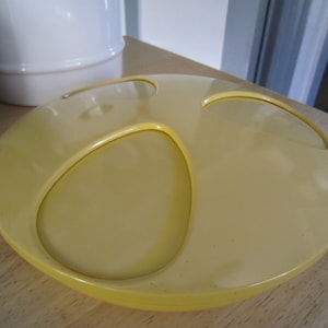 May include: A yellow ceramic dish with three round depressions. The dish is smooth and glossy.