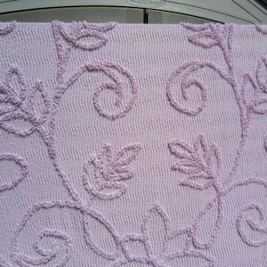 May include: A lavender-colored crocheted throw blanket with a floral pattern. The blanket features a repeating design of leaves and swirls.