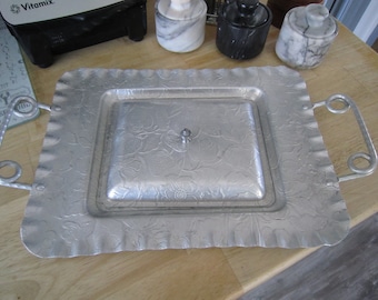 May include: A silver serving tray with a floral design and a lid. The tray has two handles on the sides.