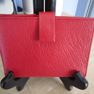 May include: A red leather wallet with a flap closure and a textured surface.